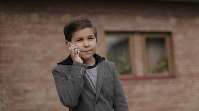 Handsome little Boy use his phone. Background of bick wall