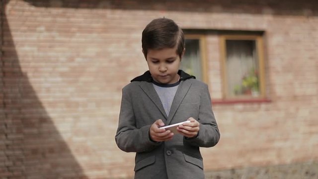 Handsome little Boy use his phone. Background of bick wall