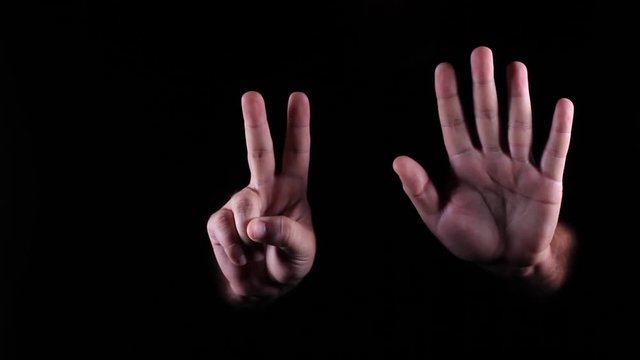 Hand Gestures coming out of the dark into the light. Holding GFX object vertically. The number 7.