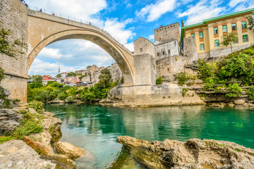 The emerald green waters of the river Neretva flow under the Mostar Bridge in the ancient city of Mostar, Bosnia and Herzegovina - obrazy, fototapety, plakaty