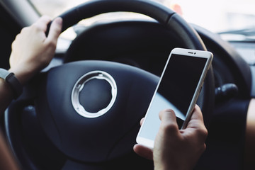 Woman sitting behind the wheel of car looking at the screen of the smartphone