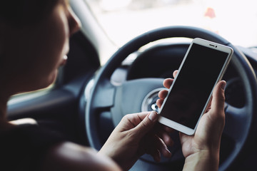 Woman sitting behind the wheel of car looking at the screen of the smartphone