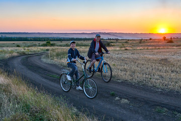 father and son ride a bike in the country on the field in the evening
