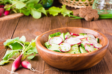 Lenten spring vegetable salad from cucumber, radish, greens and oil in a wooden plate on a wooden table