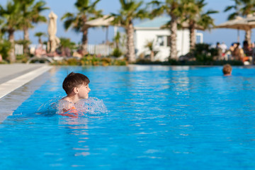 Caucasian boy in floating sleeves swimming in  pool at resort.