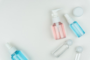 top view of the pink, blue and clear liquid containers with a white portable cream jar on white background