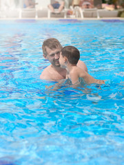 Father is teaching his son to swim in pool