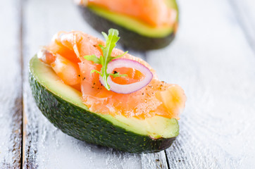 Delicious appetizer of avocado and smoked salmon on white wooden background