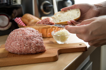 Frau schmiert Mettbrötchen mit Butter und Mett in Küche für Deutsche Brotzeit