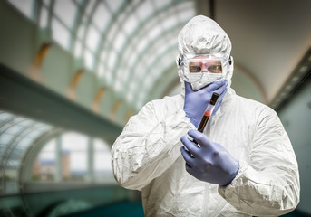 Fototapeta na wymiar Man Wearing HAZMAT Protective Clothing Holding Test Tube Filled With Blood Inside Building