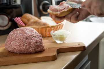 Frau schmiert Mettbrötchen mit Butter und Mett in Küche für Deutsche Brotzeit