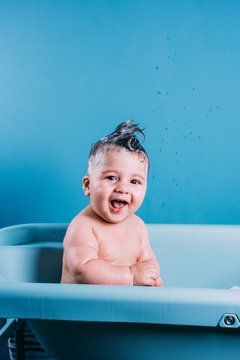 Happy laughing baby taking a bath. Smiling kid in bathroom with blue colorful background. Hygiene and care for young children.