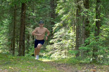 Athlete, a teenager with a bare torso, shorts and a cap running in the forest marathon distance