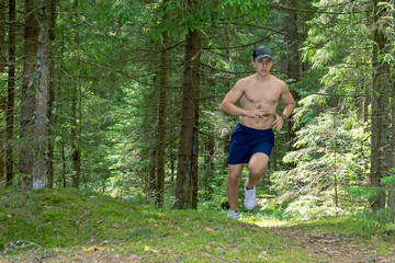 Athlete, a teenager with a bare torso, shorts and a cap running in the forest marathon distance
