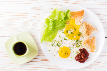 Scrambled eggs, fried bread, ketchup and lettuce leaves on a plate, coffee in a cup on the table. Ready-to-eat breakfast. Top view. Copy space