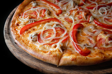 Pizza on a wooden board, with pepper, onions, chicken, cheese and tomatoes, on a black background