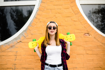 Young cheerful girl posing with yellow skateboard against orange wall