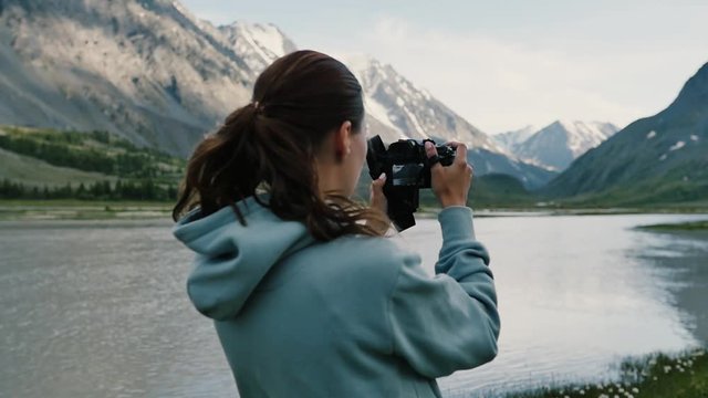 Girl takes pictures of herself against the backdrop of a beautiful mountain landscape, standing on top of a mountain. Young lady hiker standing on top of the mountain and taking a picture of valley.
