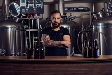 Portrait of a stylish bearded tattooed dark skinned male with crossed arms standing behind the counter in a brewery. - Powered by Adobe