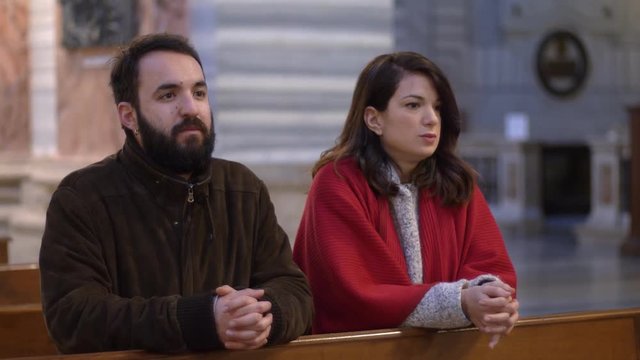 Catholic married couple praying in church to have a child