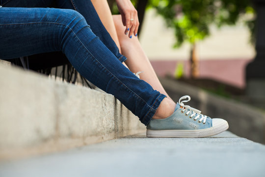 Two women sitting on stairs, one woman wearing jeans and blue sneakers, close up photo. Concept of relaxing