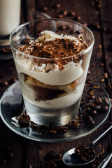 A glass of spicy latte with whipped cream and cinnamon, standing on a brown board. Coffee beans. Dark background