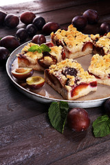 Rustic plum cake on wooden background with plums around.