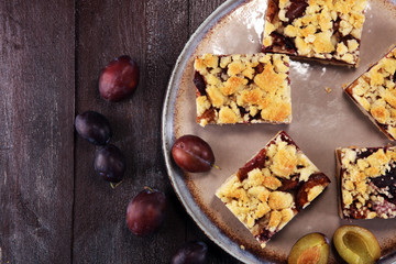 Rustic plum cake on wooden background with plums around.