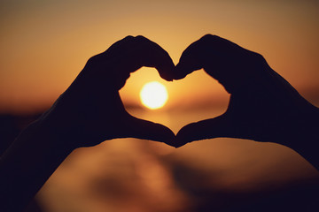 Hands in the shape of heart against the background of the sunset by the sea.