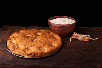 On a dark wooden table, fashionable bakeries, a bowl with flour, apricot cake and tools stand on table