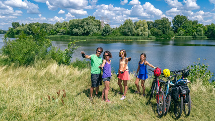 Family on bikes cycling outdoors, active parents and kids on bicycles, aerial view of happy family with children relaxing near beautiful river from above, sport and fitness concept
