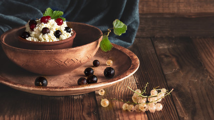 Cottage cheese and fresh berries in a clay bowl. Curd is decorated with berries of red and black currants. The dessert is in clay bowls. Top view. Daylight.