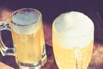 Close-up cold beers with foam and drops on old wooden table outdoor with sun beam.