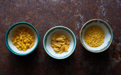 Various raw organic pasta in bowls top view