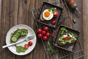Close-up of red cherry tomatoes with fresh  tostes with fried eggs on plates. Homemade breakfast, top view on vintage wooden background