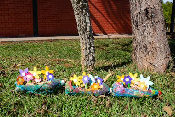 Close up of multi colored  paper flowers inside planters made of pet bottles in grass garden.