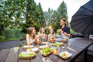 Young friends having fun sitting together with tasty snacks and drinks during the evening lights at...