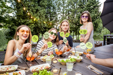 Young friends holding green plates with healthy food slogans sitting with tasty food at the outdoor cafe
