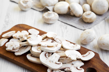 Chopped mushrooms on wooden chopping board, close-up. White wooden background. Side view.