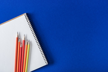 top view of various colorful pencils and blank textbook on blue background