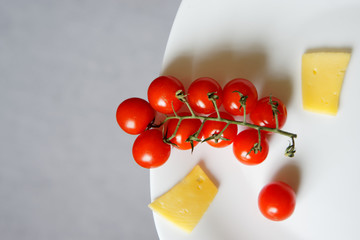 A branch of cherry tomatoes and cheese lie in a white plate