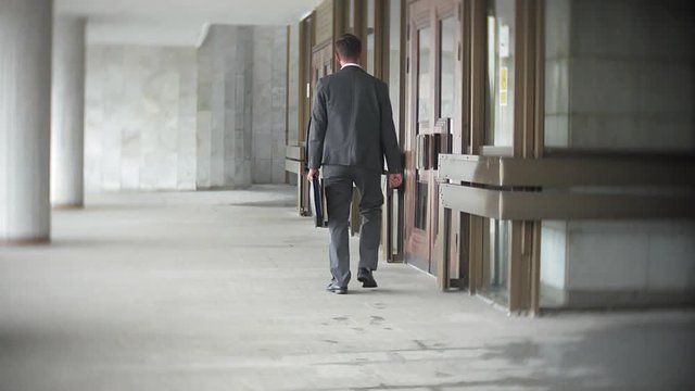 Businessman carrying briefcase while moving forward. Man in formalwear walking near modern office building, full length, copy space. Business and success concept
