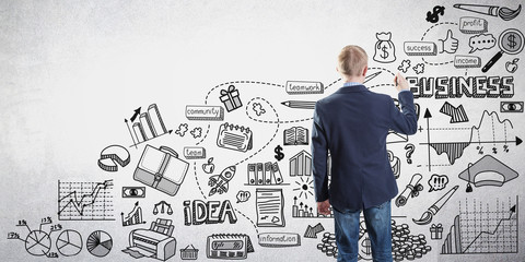 Back view of a businessman drawing a business sketch on a gray wall