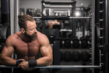 Hombre fuerte con grandes músculos descansando entre serie y serie mientras entrena en el gimnasio.