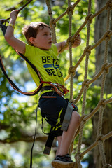 Portrait of a handsome boy on a rope park among trees. Children summer activities.