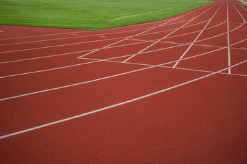 red running track background texture with white marking lanes  near green grass football field in stadium sport space