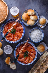 Spicy asian shrimps in tomato sauce with rice, buns and beer, top view