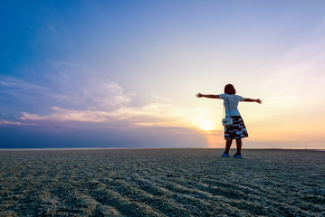Fototapeta premium Happy woman tourist arms outstretched on the beach watching the beautiful natural landscape of colorful sky and sea during sunset at Nathon Sunset Viewpoint in Samui island, Surat Thani, Thailand