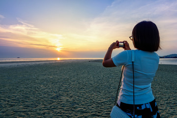 Obraz premium Asian woman tourist taking photo on the beach and beautiful natural landscape of colorful sky and sea during a sunset at Nathon Sunset Viewpoint in Samui island, Surat Thani, Thailand