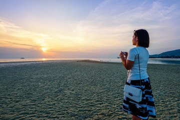 Asian woman tourist taking photo on the beach and beautiful natural landscape of colorful sky and sea during a sunset at Nathon Sunset Viewpoint in Samui island, Surat Thani, Thailand